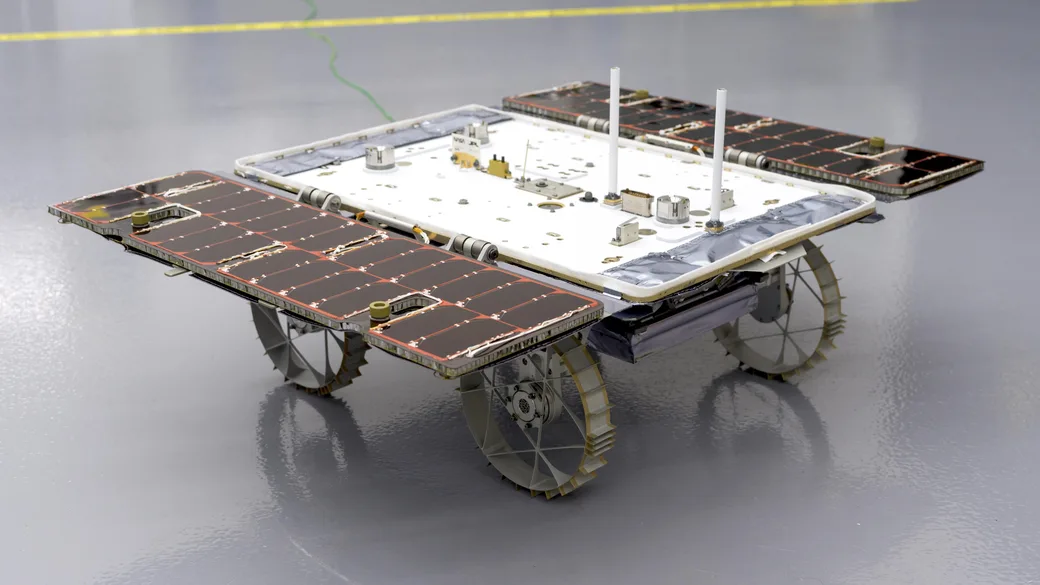 A CADRE research rover with solar panels, antennas and metal wheels in a clean room.